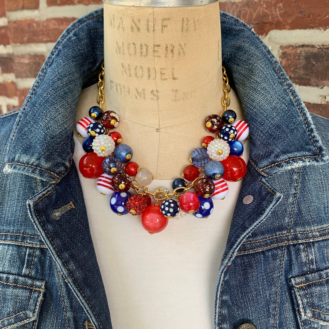 Patriotic charm necklace filled with an assortment of red, white, and blue beads. Chunky charm necklace with dangling beads hanging from gold chain. 