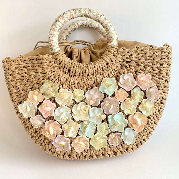 Tan half moon straw handbag embellished with pastel painted seashells and cream pearls. Round top handle straw totes for summer.