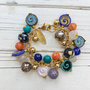 Ammonite charm bracelet with assorted colorful beads dangling from a gold bracelet chain. Colorful bracelet for women.