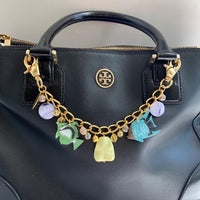 Gold fish bag chain hanging on a black handbag. Fish bag chain with blue and green tropical fish charms, round blue beads, and rhinestone ball beads. Fish bag charm.