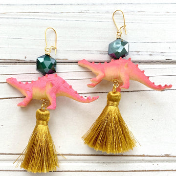 Cute dinosaur earrings for women with miniature pink dinosaurs topped with a dark green faceted bead, and a gold silk thread tassel hanging below. Dino earrings. 