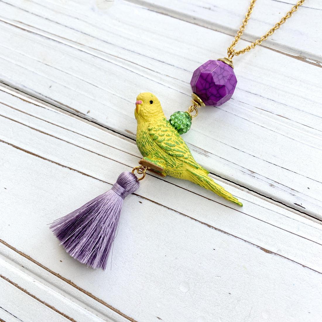 Parakeet pendant necklace for women. Yellow parakeet pendant with purple tassel, green rhinestone beads, purple crackle bead hung on a gold chain.